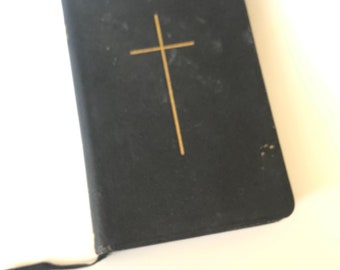 May include: A black, worn leather-bound book with a gold cross embossed on the front cover. The book has a black ribbon bookmark.