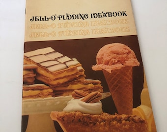 May include: A vintage cookbook titled "JELL-O PUDDING IDEABOOK" with a retro design. The cover features images of desserts, including layered pastries, a scoop of ice cream in a cone, and a pecan pie. The color palette includes brown, beige, and cream.