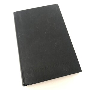 May include: A closed, rectangular black book with a slightly worn cover. The book is set against a white background, with the spine visible on the left side. The cover shows minor wear and tear.
