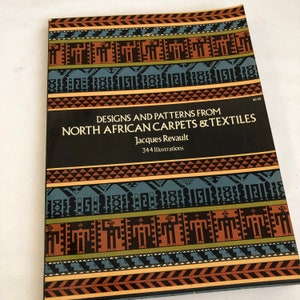 May include: A book cover with a black background and colorful geometric patterns. The title is "Designs and Patterns from North African Carpets & Textiles" by Jacques Revault. The book features 344 illustrations.