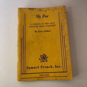 May include: A vintage book cover for "Sly Fox," a comedy in two acts adapted from "Volpone" by Larry Gelbart. The cover is yellowed with age, featuring black text and a lion emblem. Published by Samuel French, Inc.