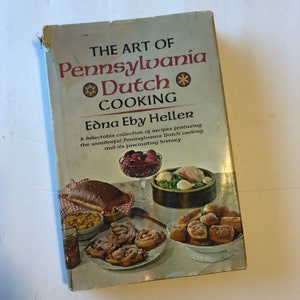 May include: A vintage cookbook titled "The Art of Pennsylvania Dutch Cooking" by Edna Eby Heller. The cover features the title in red and black, with illustrations of various dishes. The book's cover is slightly worn.