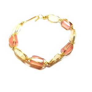 May include: A gold wire wrapped bracelet with pink gemstone beads.