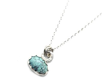 May include: A silver necklace with a turquoise stone pendant. The pendant is surrounded by a silver ring and a silver chain.
