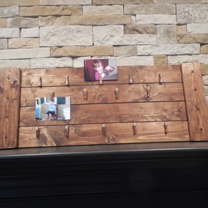 May include: A rustic wooden photo display with clips for holding pictures. The display has a dark brown stain and is made of reclaimed wood. There are two photos in the display, one of a child and one of an older person.