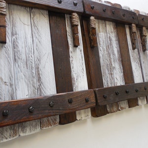 May include: Rustic wooden wall decor with a whitewashed finish. The decor features multiple sections with rope accents and metal hardware.