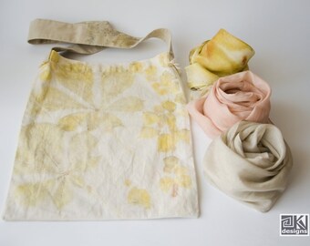 May include: A white fabric tote bag with a yellow and brown leaf pattern. The bag has a brown leather strap. Three silk scarves in yellow, pink, and beige are arranged next to the bag.