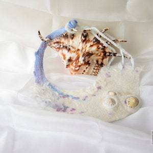May include: A white felted fabric necklace with a seashell design. The necklace is decorated with small seashells and has a blue and purple gradient.