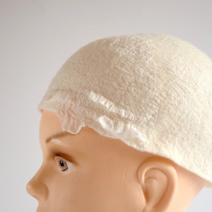 May include: A white felt hat with a ruffled edge. The hat is on a mannequin head.