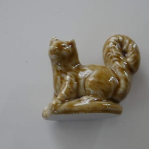 May include: A brown ceramic figurine of a cat with a curled tail. The cat is sitting on a base and has a detailed, textured surface.