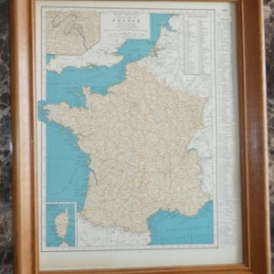 May include: Framed vintage map of France, featuring a detailed depiction of the country's geography. The map is set against a light blue background, with a wooden frame. The map includes the text "FRANCE" at the top.