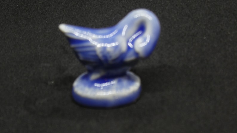 May include: A small, ceramic figurine of a swan in shades of blue and white. The swan has a curved neck and is perched on a round base. The figurine is likely a decorative item.