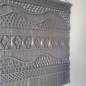 May include: Gray macrame wall hanging with a wave pattern and fringe.