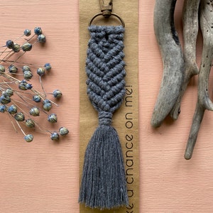 May include: Grey macrame keychain with a tassel and a metal key ring. The keychain is attached to a brown card with the text "Take a chance on me!"