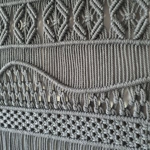 May include: Gray macrame wall hanging with a geometric pattern and fringe.