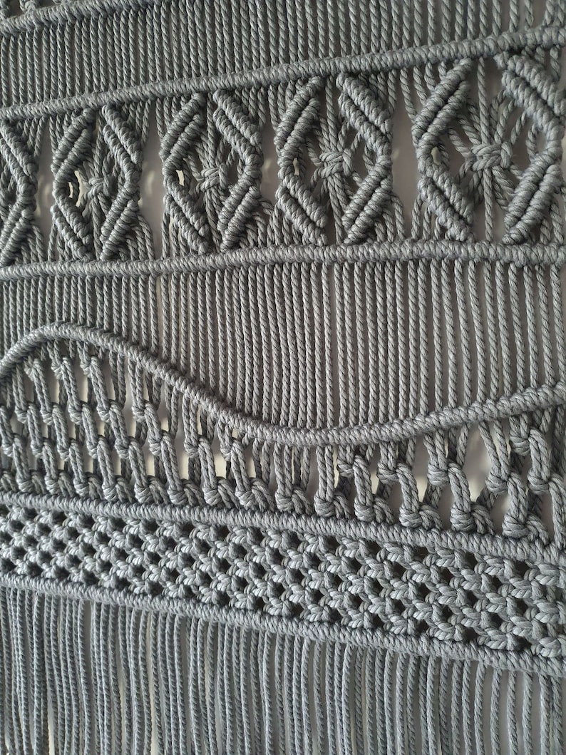 May include: Gray macrame wall hanging with a geometric pattern and fringe.
