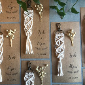 May include: A set of six white macrame keychains with a tassel on the bottom. Each keychain is attached to a brown card with the text "Jpek & Alper" and the date "06.04.2019".