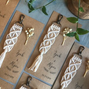 May include: White macrame keychains with a tassel on a brown card with the text "Ipek & Alper 06.04.2019" printed on it.