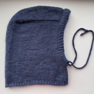 May include: A knitted blue balaclava with a rounded top and a face opening. The balaclava has a ribbed edge around the face and a drawstring. The knitted fabric has a textured appearance.
