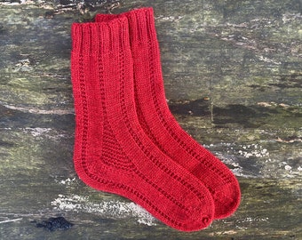 May include: A pair of red knitted socks with a textured pattern. The socks are laid flat on a wooden surface.