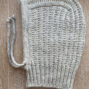 May include: A gray knitted hooded hat with a long tie string. The hat is made of a soft, textured yarn.