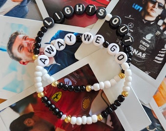 Puede incluir: Dos pulseras de cuentas con cuentas negras y blancas y detalles dorados. Las pulseras deletrean "Lights Out Away We Go".