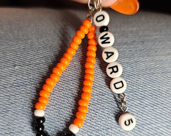 Pode incluir: Chaveiro de contas laranja e preto com o nome "WARD" e o número "5" em contas brancas.