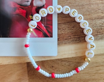 May include: White beaded bracelet with red beads and gold lettering spelling "LORD ♥ PERCEVAL".