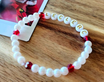 May include: White beaded bracelet with red beads and gold lettering spelling "LECLERC".