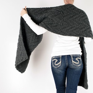 May include: A charcoal grey crocheted scarf draped over a person's shoulders. The scarf is long and wide, and it has a textured, chunky knit.