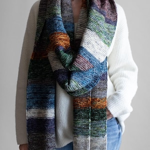 May include: A colorful, striped scarf in shades of blue, green, orange, and purple. The scarf is knitted and appears soft and warm. The scarf is wrapped around the neck and shoulders.