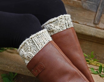 May include: A pair of brown leather boots with white knitted boot cuffs. The cuffs are made with a chunky yarn and have a cable knit pattern.