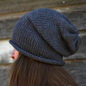 May include: A dark grey slouchy beanie hat made of knitted fabric. The hat has a folded brim and is being worn on someone's head.