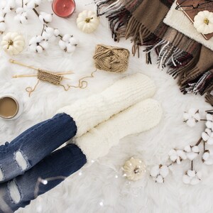 May include: A pair of white fluffy socks with a pair of blue jeans on a white fluffy surface. There are cotton balls, yarn, and a small pumpkin on the surface.