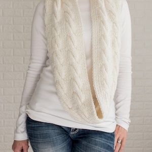 May include: A white knitted infinity scarf with a cable knit pattern.