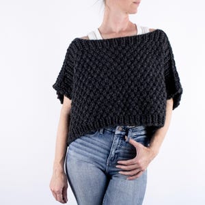 May include: A dark gray knitted sweater with a textured pattern and short sleeves. The sweater is cropped and has a relaxed fit.