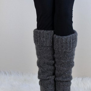 May include: Grey knitted leg warmers with a fold-over cuff. The leg warmers are worn over black leggings and black ankle boots.