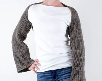 May include: A brown knitted arm warmer with long sleeves. The arm warmer is worn over a white t-shirt and blue jeans.