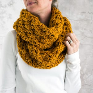 May include: A mustard yellow crocheted infinity scarf. The scarf is thick and chunky and has a cable knit pattern.
