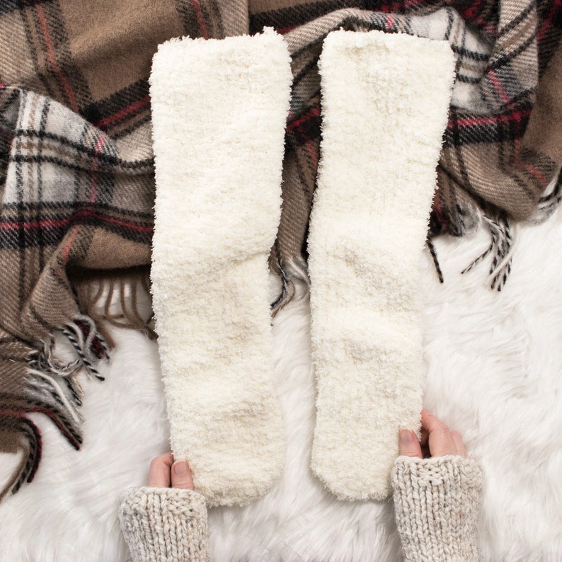 May include: Two pairs of white fluffy socks on a white fluffy surface. The socks are made of a soft, plush material and are perfect for keeping your feet warm in the winter.