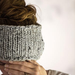 Pode incluir: Uma faixa de cabeça de malha cinza com uma superfície texturizada. A faixa de cabeça está sendo usada por uma pessoa com cabelo castanho.