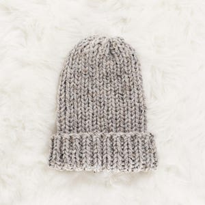 May include: A grey knitted beanie hat with a textured pattern. The hat is folded down at the brim.