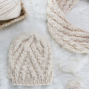 May include: A cream-colored knitted hat and scarf set with a cable knit pattern. The hat and scarf are made of soft yarn and have a cozy, wintery feel.