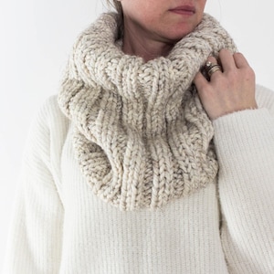 Könnte beinhalten: Ein dicker Strick-Kragenpullover in Cremefarbe. Der Schal ist aus weichem, strukturiertem Garn gefertigt und perfekt, um sich im Winter warm zu halten.