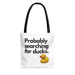 May include: White tote bag with black handles and the text "Probably searching for ducks." with a yellow rubber duck illustration.