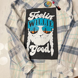 May include: A blue and white plaid flannel shirt with a black patch on the back that says "Feelin' Willie Good" with a cartoon image of Willie Nelson wearing sunglasses and a bandana.