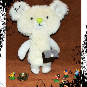 May include: A white plush teddy bear with a green nose and a gray purse. The bear is sitting on a brown surface with several small, colorful bird figurines.