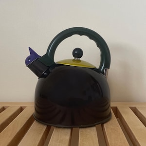 May include: A black kettle with a green handle and a yellow lid. The kettle has a purple whistle on the spout.