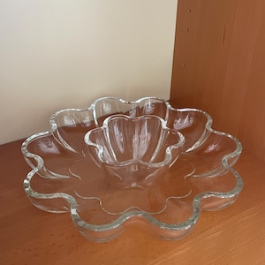 Puede incluir: Un juego de fuentes de vidrio transparente. El juego incluye una fuente grande en forma de flor con borde festoneado y un cuenco más pequeño a juego en el centro. El vidrio es transparente.