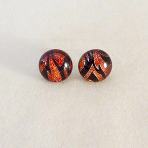 May include: A pair of round stud earrings. Each earring is a dark, glossy sphere with a pattern of red and orange streaks against a black background. The earrings are set against a plain, off-white backdrop.